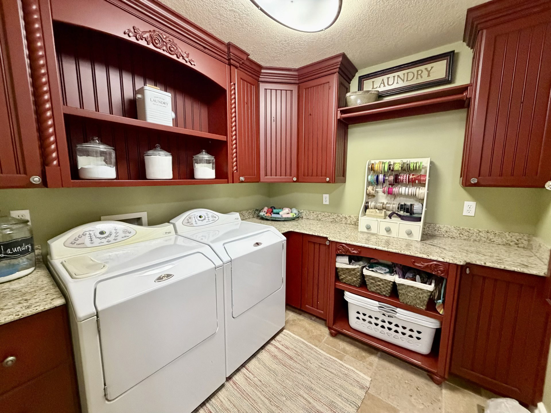Laundry area featuring extensive red-stained cabinetry with carved details, an open display shelf, and granite-finish countertops