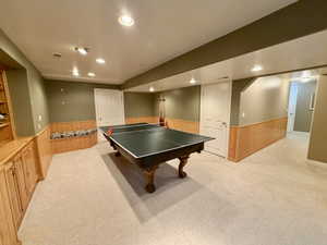Spacious recreation room featuring a ping-pong table, recessed lighting, wall-to-wall carpeting, wood-paneled wainscoting, and built-in cabinetry with shelving