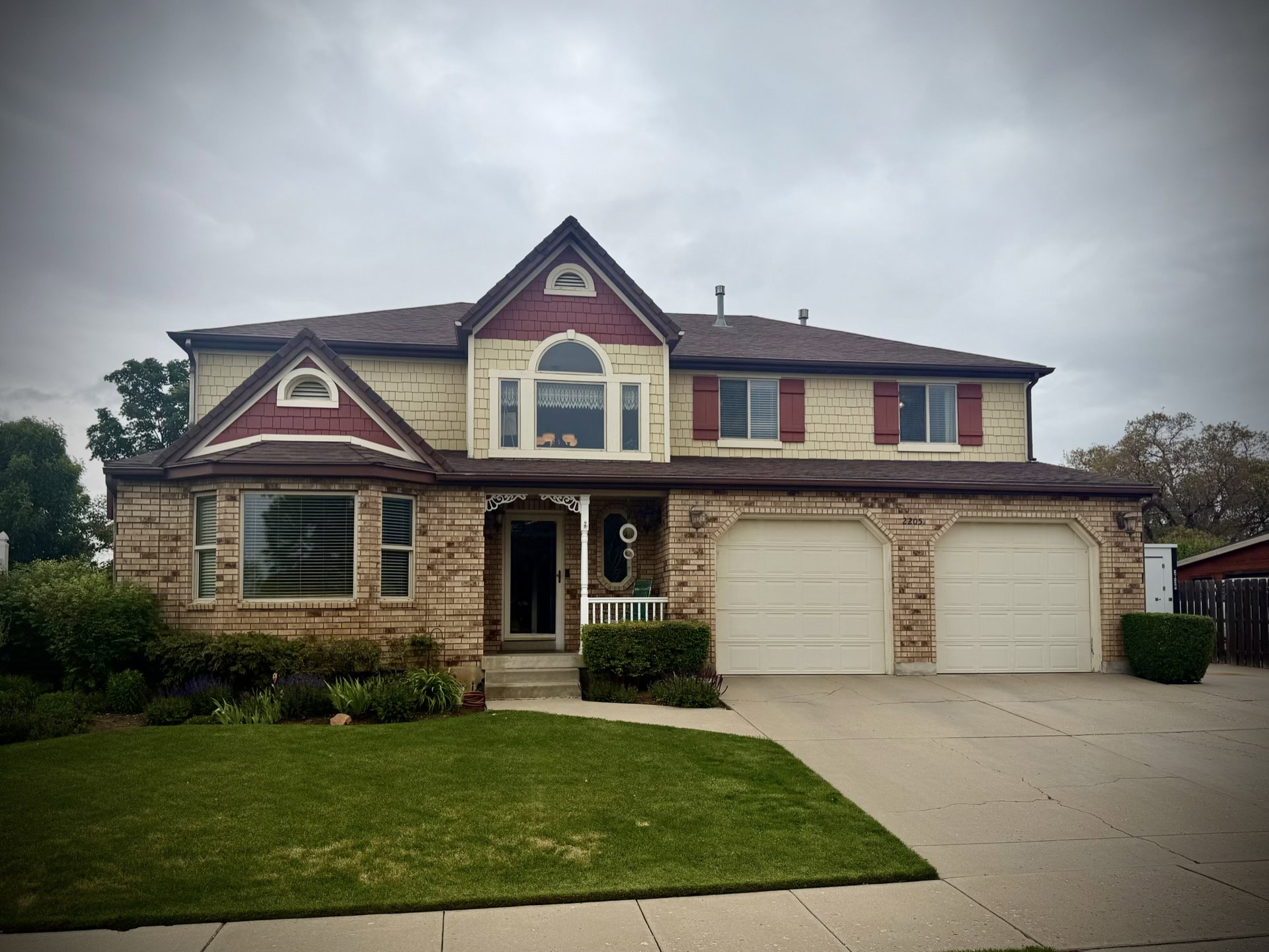 Two-story residence featuring brick and shingle siding with dark red trim accents