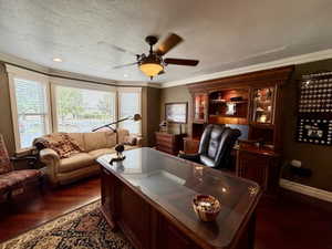 Dedicated room featuring rich wood-finish flooring, a prominent bay window with blinds, a built-in wood-finish cabinet with display lighting, and a ceiling fan with integrated lighting