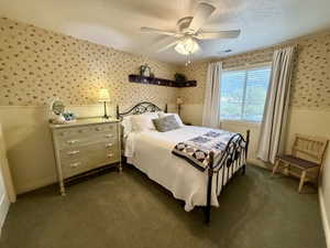 Carpeted room featuring a ceiling fan with integrated lighting, a window with blinds and drapes, and wainscoting with patterned wallpaper above
