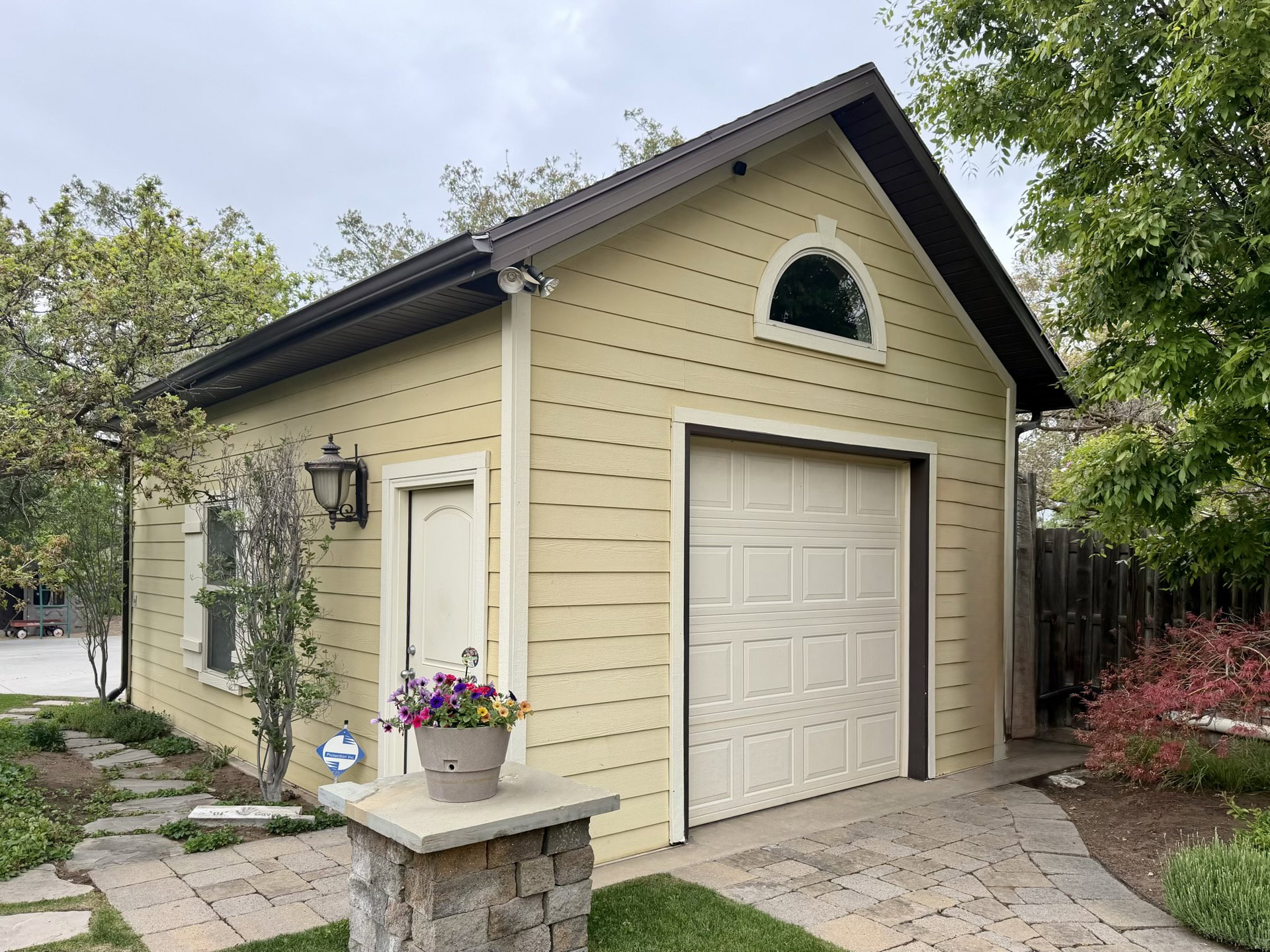 Yellow horizontal siding exterior with a peaked roofline, featuring a single garage door, an arched window, and a side entry door