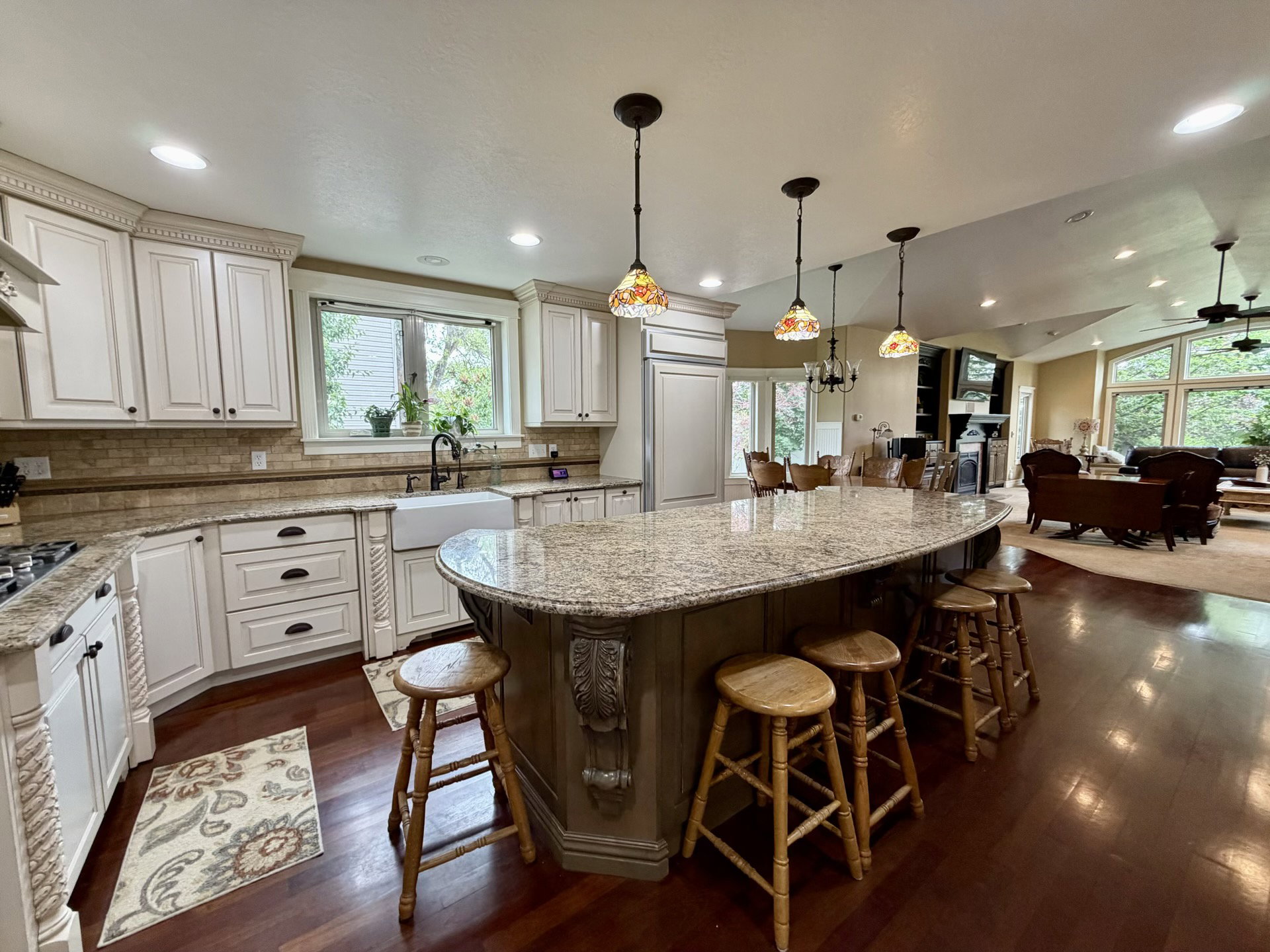 Kitchen featuring a curved central island with an extended granite countertop, white cabinetry with decorative molding, a farmhouse sink, and wood-finish flooring