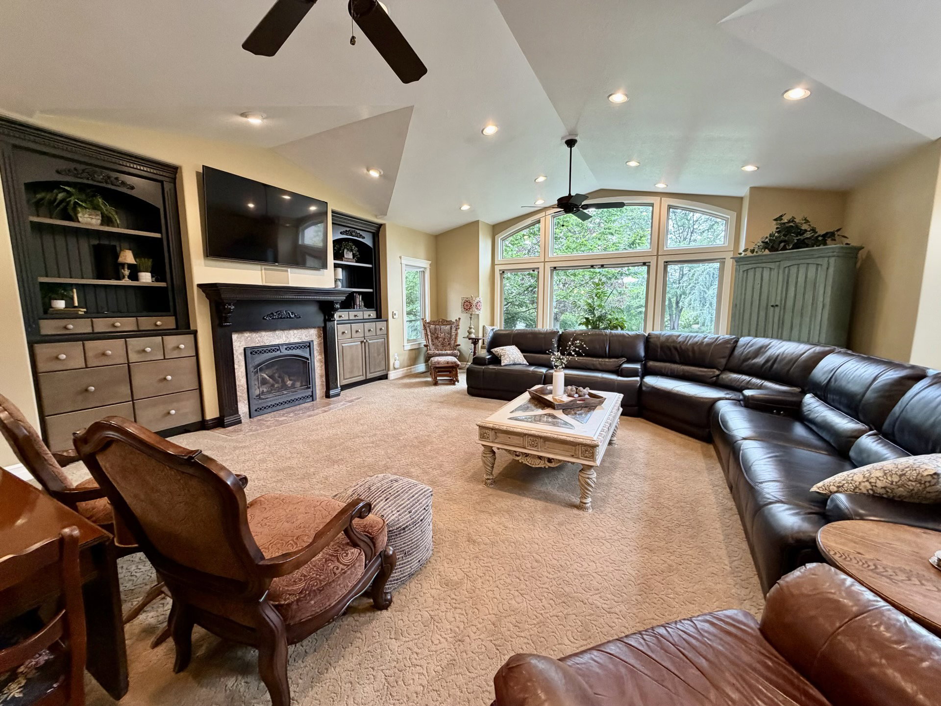 Spacious living area featuring a vaulted ceiling with recessed lighting, an arched window wall, a fireplace with a stone surround, and built-in cabinetry