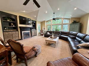 Spacious living area featuring a vaulted ceiling with recessed lighting, an arched window wall, a fireplace with a stone surround, and built-in cabinetry