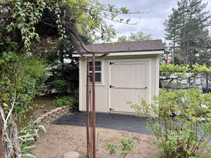 Utility shed with beige siding, a brown shingle roof, and a single window
