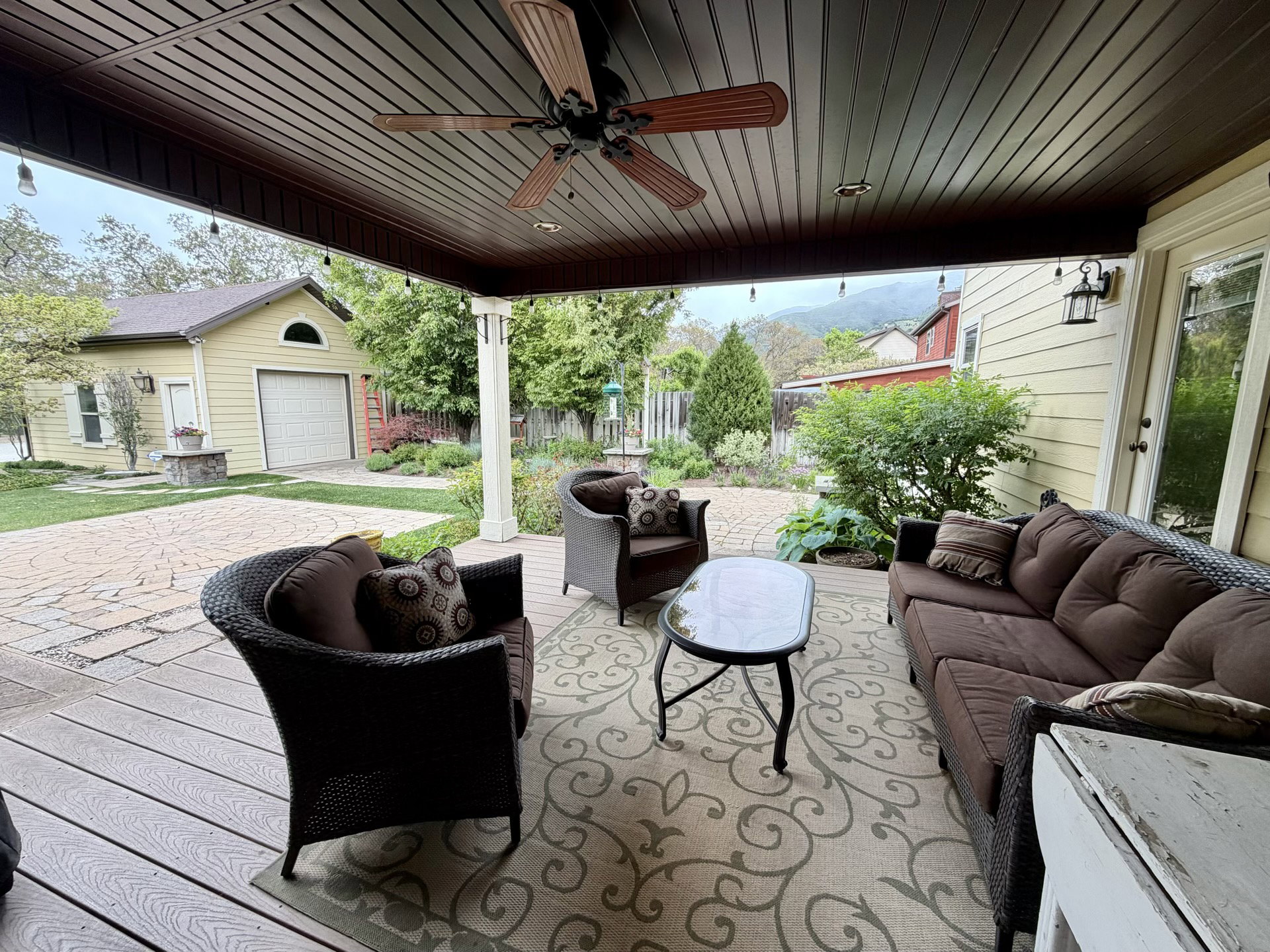 Covered outdoor patio featuring a wood-finish slatted ceiling, ceiling fan with light, and string lighting