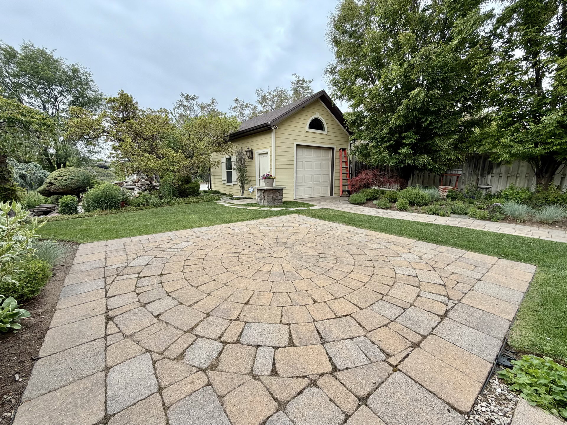 Circular paver patio with a contrasting border, surrounded by manicured lawn and mature landscaping