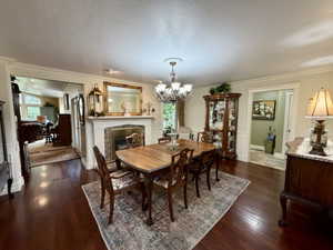 Formal dining area featuring rich wood-finish flooring, a fireplace with a mantel, crown molding, and wainscoting