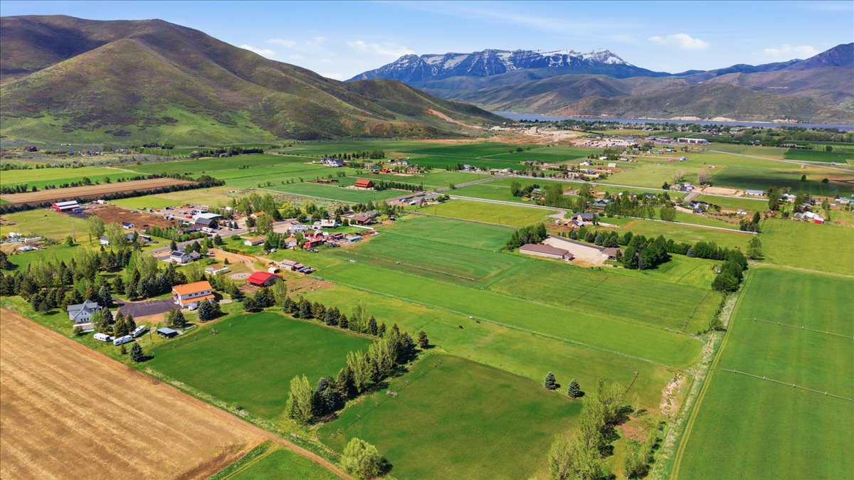 Expansive rural landscape featuring verdant fields, scattered residential properties, and distant snow-capped mountains