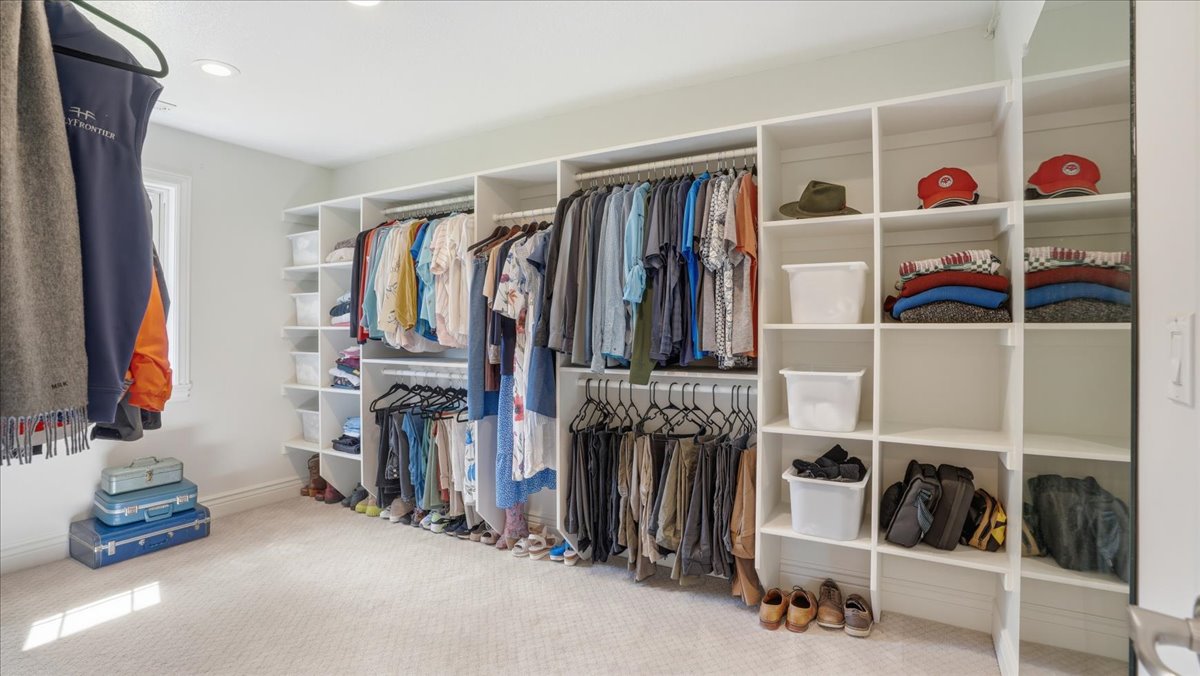 Custom closet organization system featuring white shelving, multiple hanging rods, built-in cubbies, and a full-length mirror