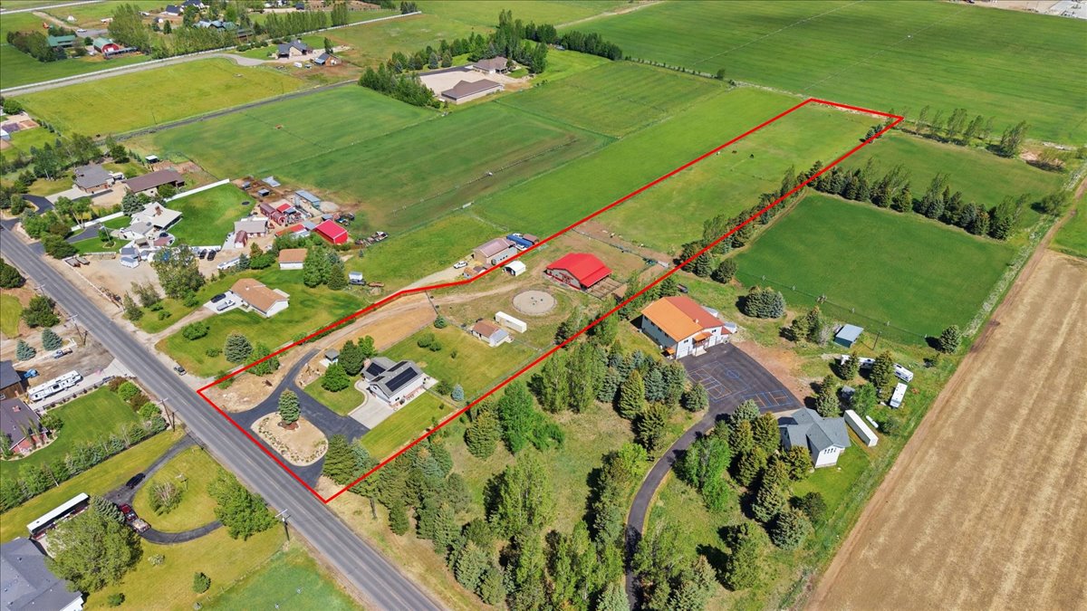 Expansive agricultural property featuring multiple structures, paved driveways, a large red barn, and extensive green fields