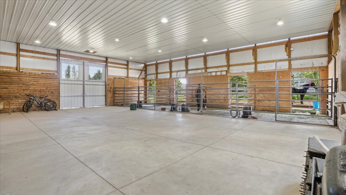 Spacious interior barn featuring a concrete floor, a metal ceiling, multiple stalls with metal gates, and large double-door entry