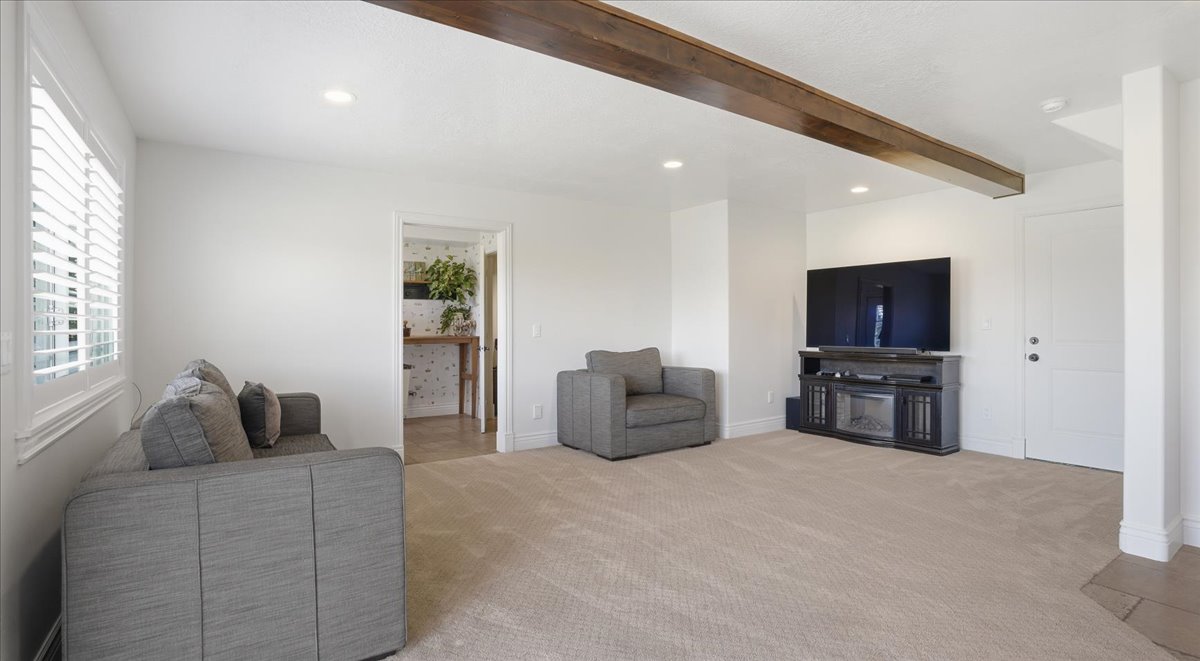 Spacious living area featuring neutral carpeting, recessed lighting, and a prominent wood-finish beam