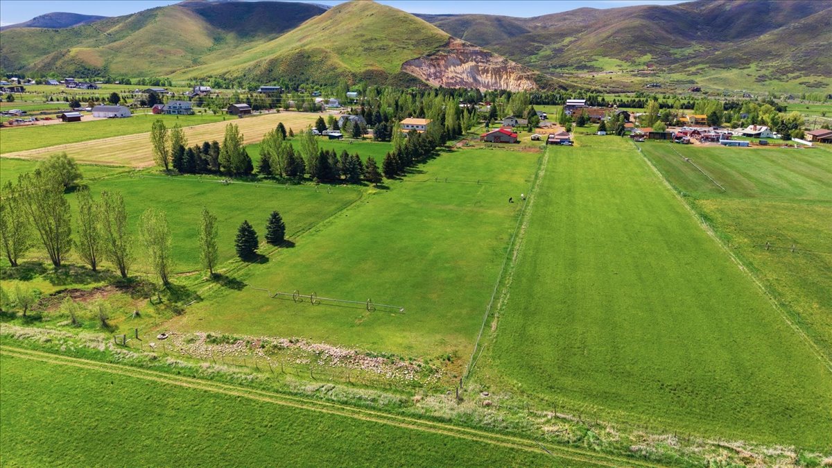 Expansive green fields featuring natural landscaping, bordered by mature trees and distant foothills