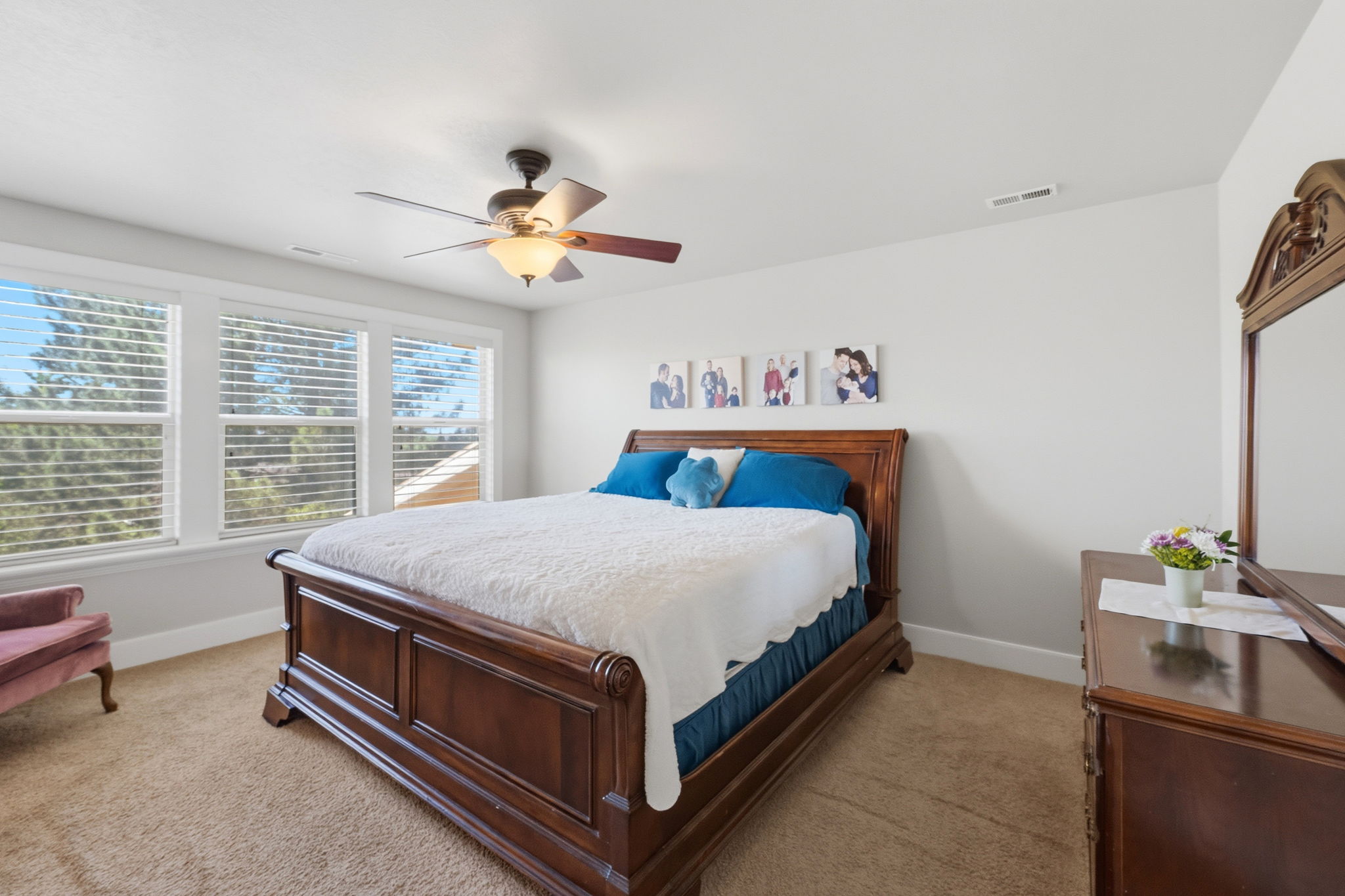 Bedroom featuring a triple window bank, neutral wall paint, and a ceiling fan with integrated lighting
