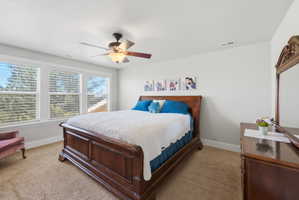 Bedroom featuring a triple window bank, neutral wall paint, and a ceiling fan with integrated lighting