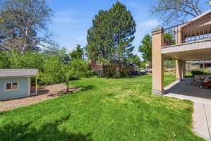 Expansive backyard featuring a lush lawn, mature trees, a dedicated shed, and a covered patio area