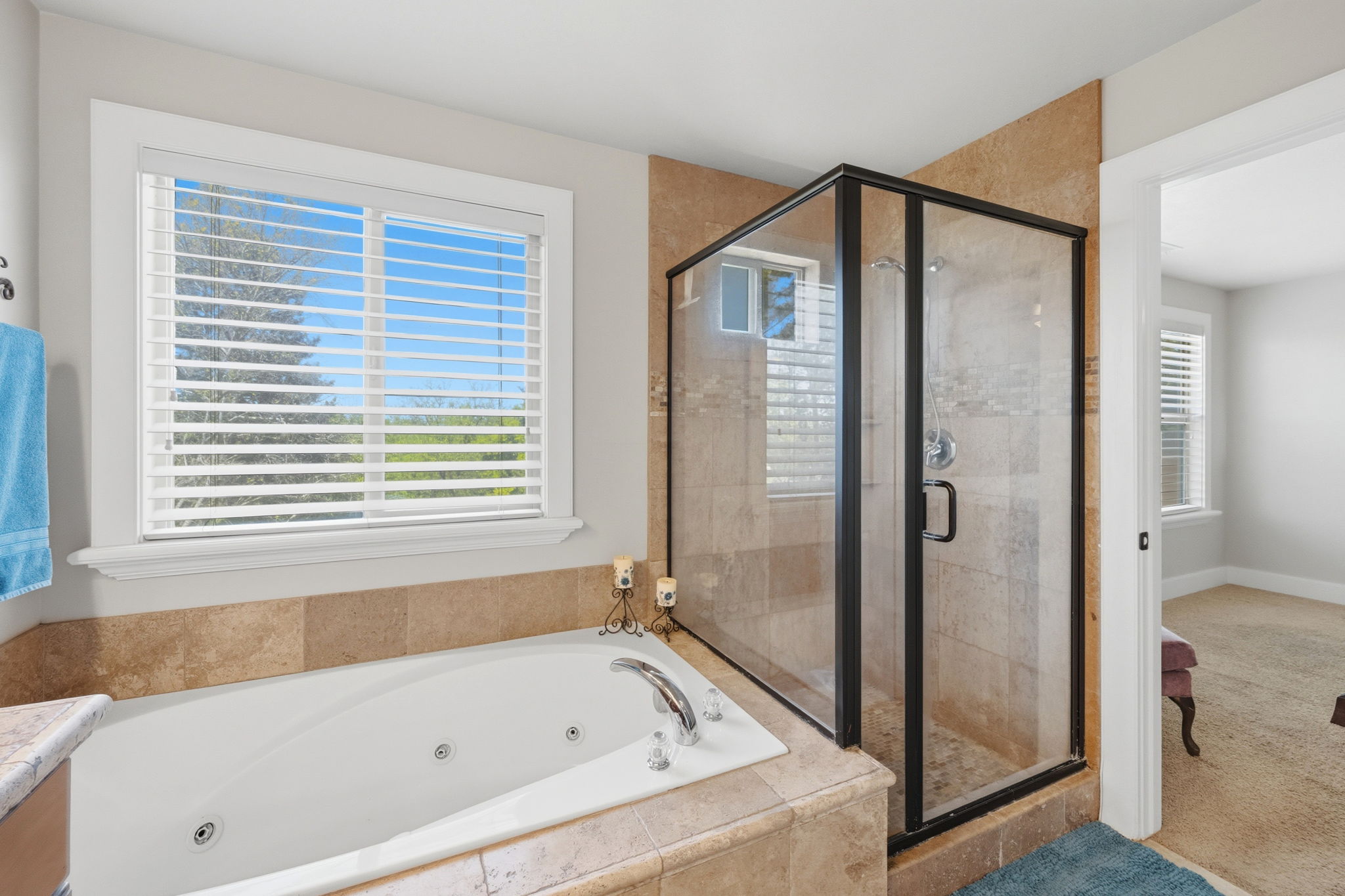 Bathroom featuring a jetted soaking tub, a glass-enclosed shower with tiled walls, and a window with blinds