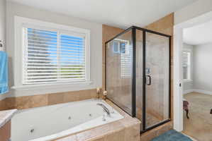 Bathroom featuring a jetted soaking tub, a glass-enclosed shower with tiled walls, and a window with blinds