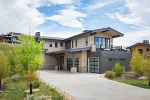Contemporary residence featuring a multi-tone exterior, expansive upper-level balcony, and a paved driveway