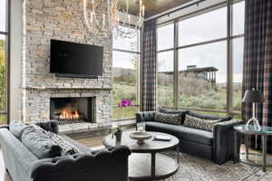 Living area featuring a floor-to-ceiling stone fireplace, expansive windows, wood-paneled ceiling, and a prominent chandelier