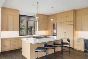 Modern kitchen featuring light wood-finish cabinetry, a large center island with counter seating, integrated appliances, and a built-in beverage refrigerator