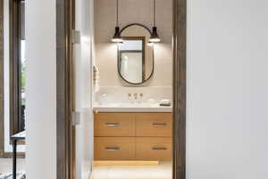 Powder room featuring a wood-finish vanity with four drawers, a white countertop with an undermount sink, and a black-framed oval mirror