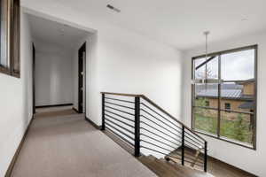 Modern staircase featuring wood-finish treads, a black metal horizontal bar railing, and a contemporary chandelier