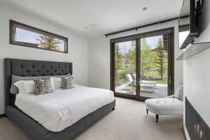 Carpeted room featuring a horizontal window, wood-frame sliding glass doors opening to a concrete patio, and a built-in wall-mounted fireplace