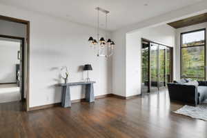 Spacious interior with dark wood-finish flooring, white walls, and a silver-toned chandelier featuring black shades