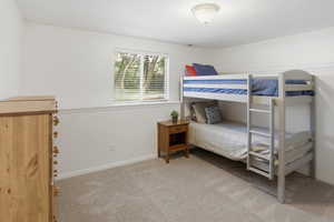 Carpeted interior space featuring white walls with chair rail molding and a single window with blinds