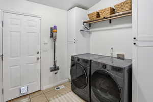 Dedicated laundry area featuring modern front-loading appliances, white cabinetry, a wood shelf with integrated hanging rod, and tile flooring