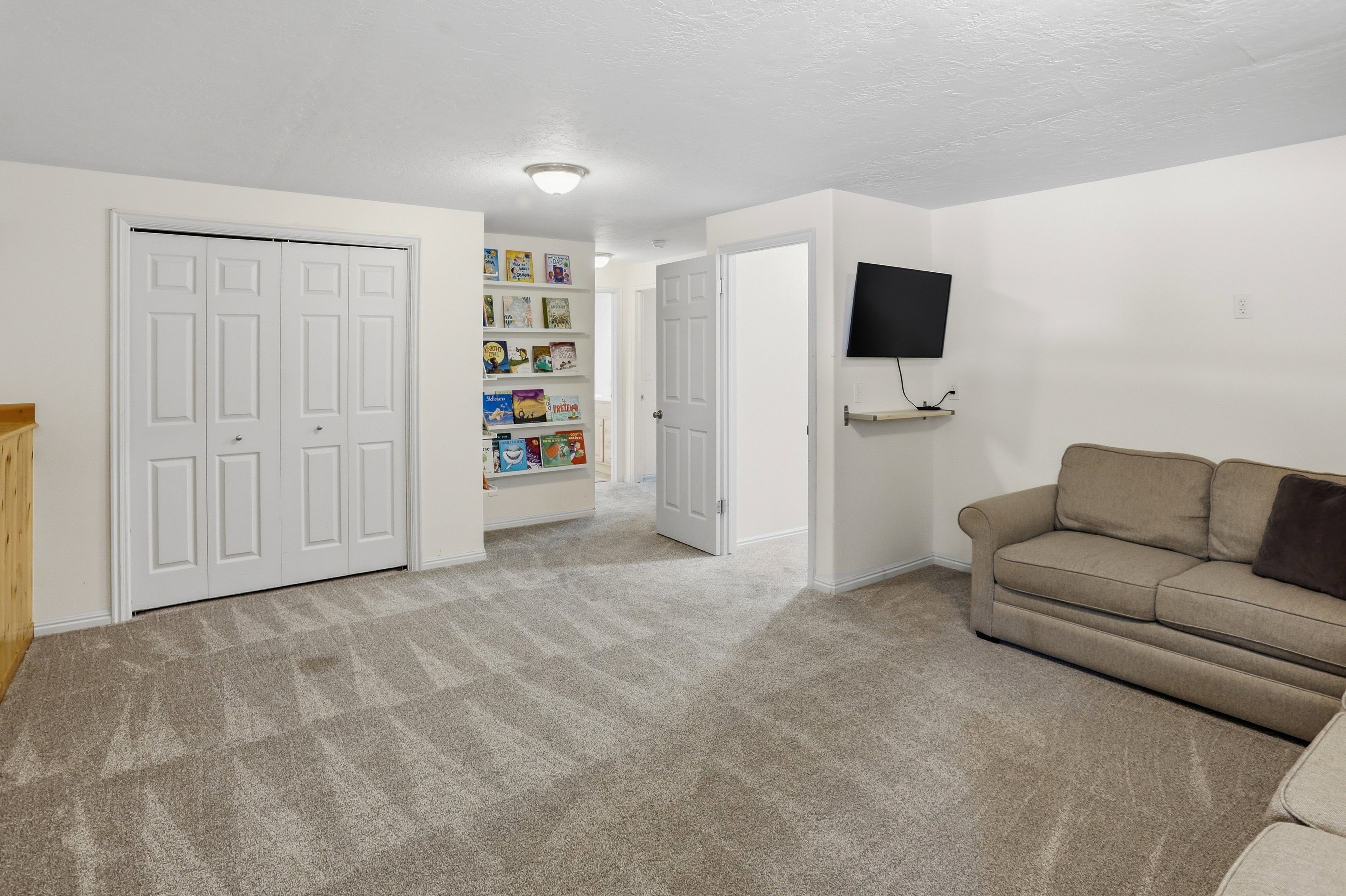 Carpeted room featuring a built-in shelving unit, a wall-mounted floating shelf, and a closet with bifold doors
