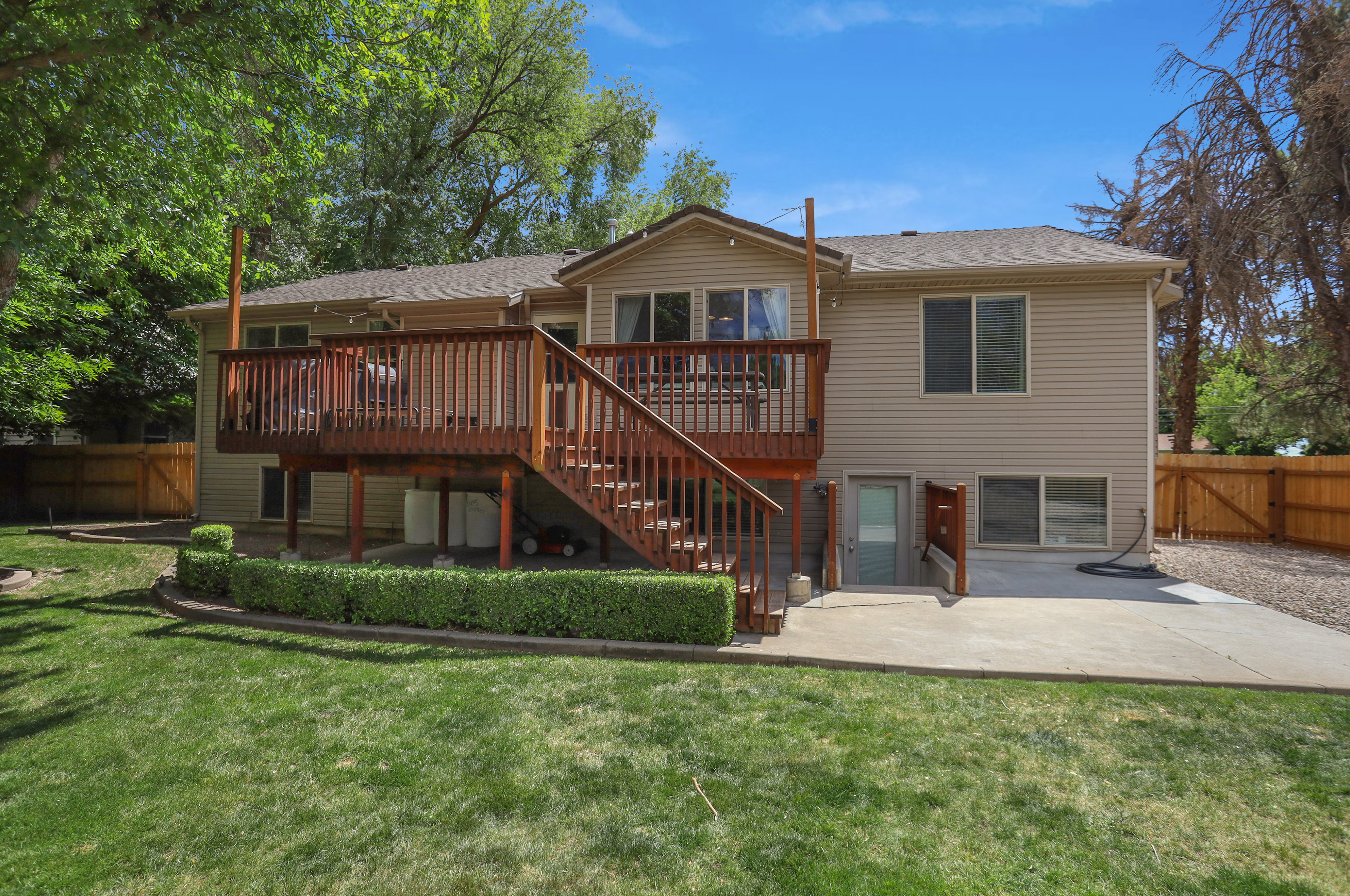 Expansive backyard featuring a large elevated wood deck with stairs, a ground-level concrete patio, mature trees, and a manicured lawn