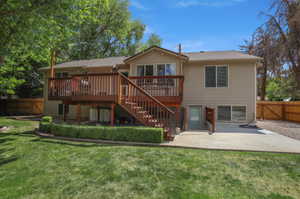 Expansive backyard featuring a large elevated wood deck with stairs, a ground-level concrete patio, mature trees, and a manicured lawn