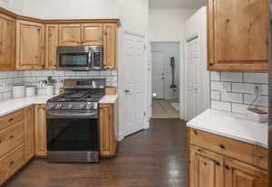 Kitchen featuring wood cabinetry, white countertops, subway tile backsplash, stainless steel gas range, and matching microwave