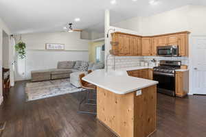 Kitchen featuring warm wood-finish cabinetry, white subway tile backsplash, stainless steel appliances, a center island with seating, and wood-finish flooring