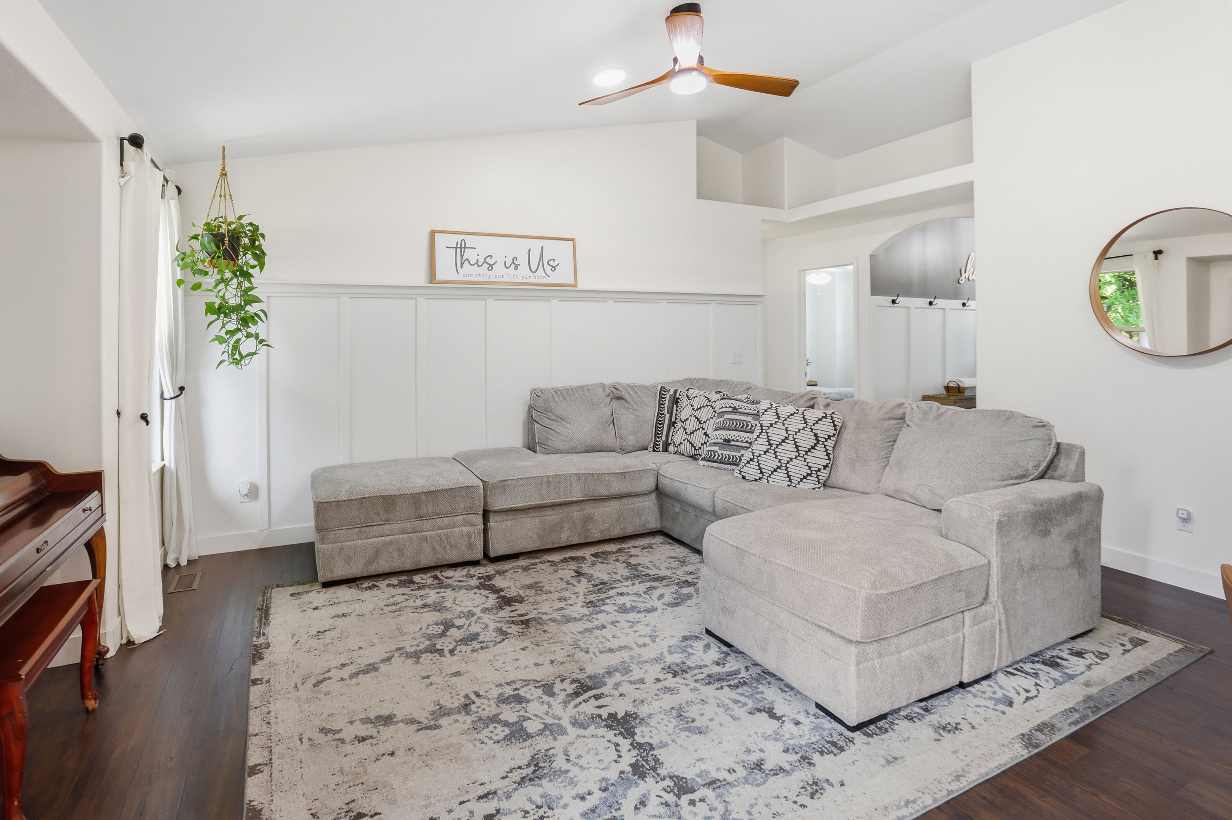Living area featuring rich wood-finish flooring, white board and batten wall detailing, and a modern ceiling fan