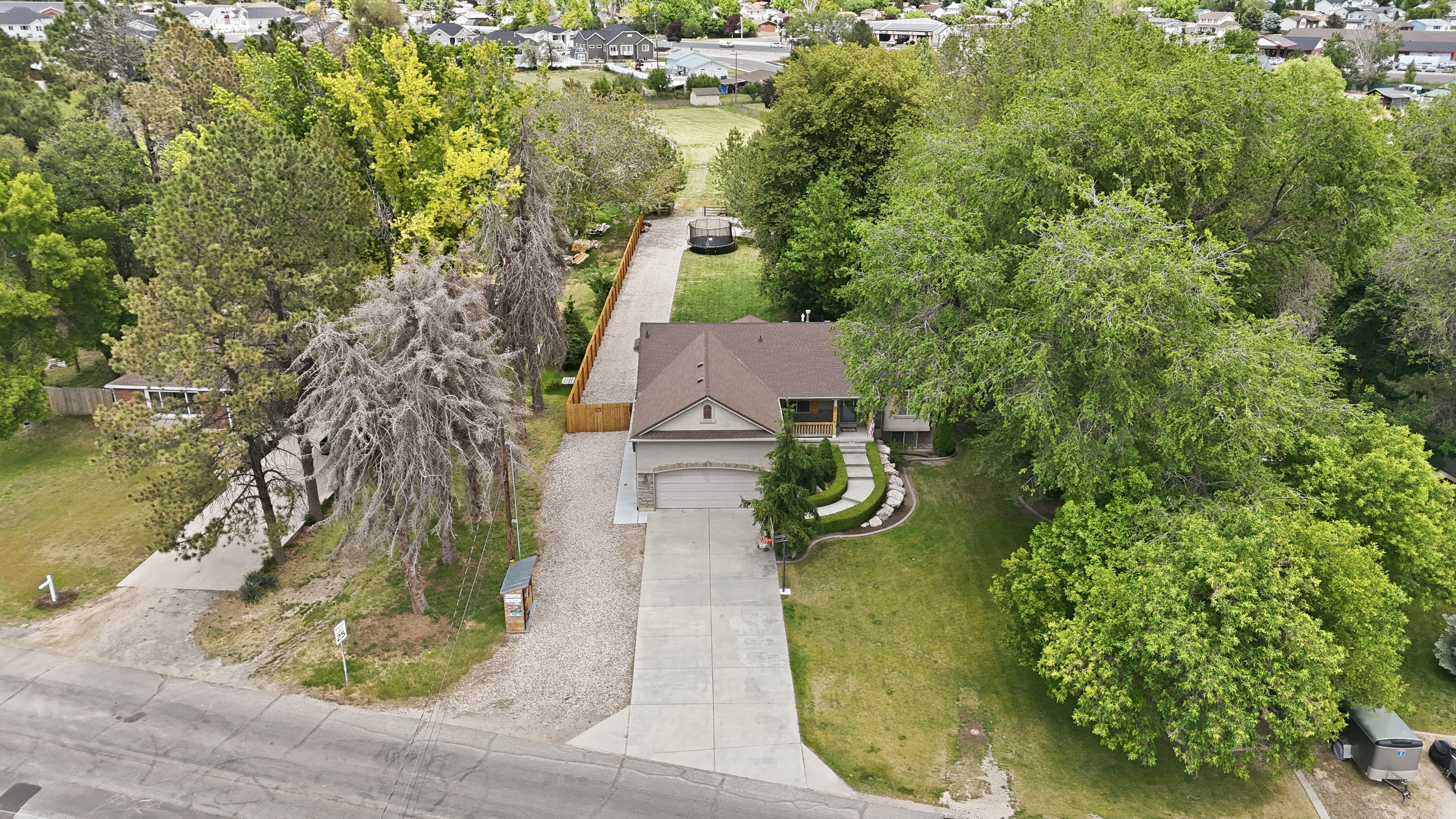 Expansive property featuring a two-car garage, mature trees, manicured lawns, and a long concrete driveway
