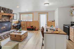 ADU open-concept living space in basement apartment featuring a stone fireplace with a substantial wood mantel, light wood-finish flooring, and natural wood wainscoting