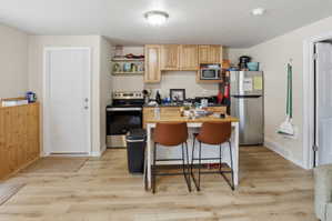 Basement apartment kitchen area featuring stainless steel appliances, wood-finish flooring, light wood cabinetry, and an island with seating