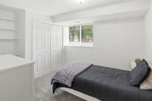 Bright interior space featuring a window with horizontal blinds, built-in shelving, bi-fold closet doors, and light grey carpet flooring