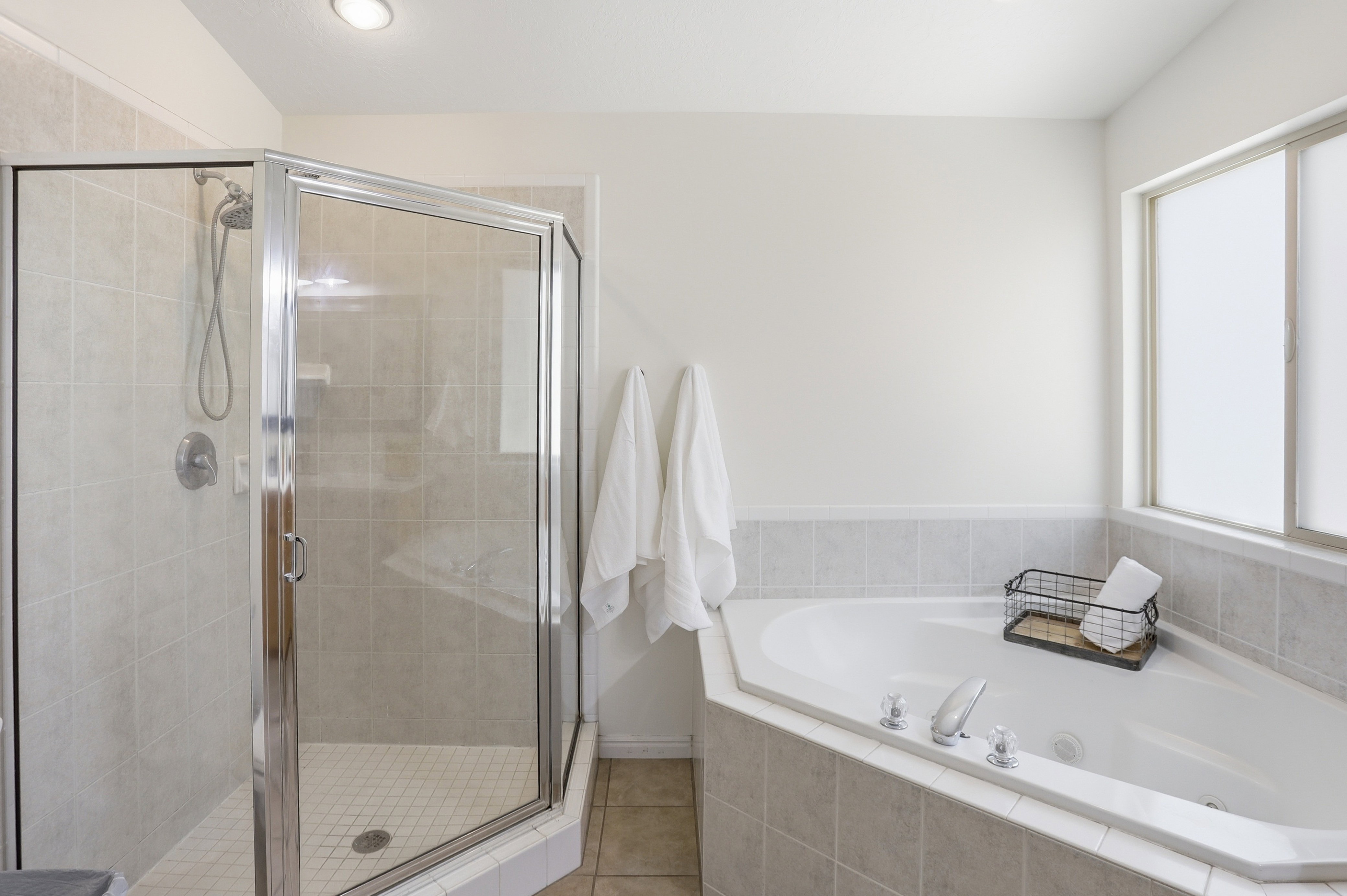 Corner soaking tub with integrated tiled surround, frosted window, and adjacent glass-enclosed shower featuring a tiled interior and built-in shelf