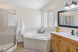 Master bathroom featuring a corner soaking tub with tile surround, a glass-enclosed shower with tile walls, a vanity with wood cabinetry and a white countertop, and a large mirror with a dark frame
