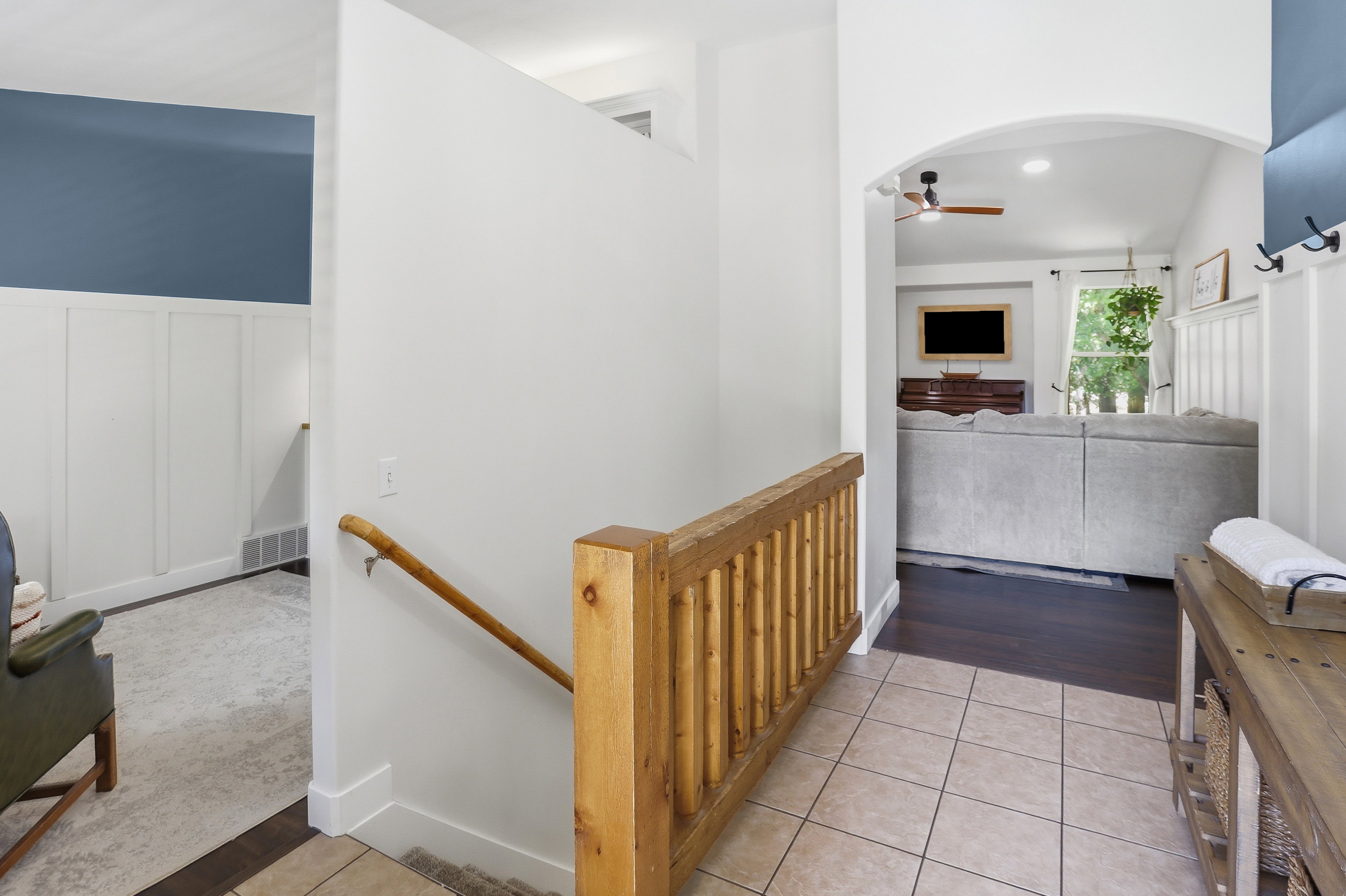 Entryway featuring ceramic tile flooring, a wood balustrade with a handrail, and an arched doorway leading to a living area with wood-finish flooring
