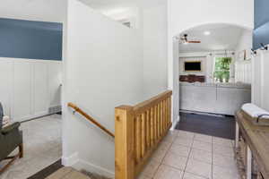 Entryway featuring ceramic tile flooring, a wood balustrade with a handrail, and an arched doorway leading to a living area with wood-finish flooring