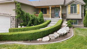 Front exterior featuring varied landscaping with manicured hedges, decorative boulders, and mature plantings