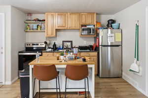 Kitchen featuring wood-finish flooring, natural wood cabinetry, stainless steel appliances, and a central island with seating