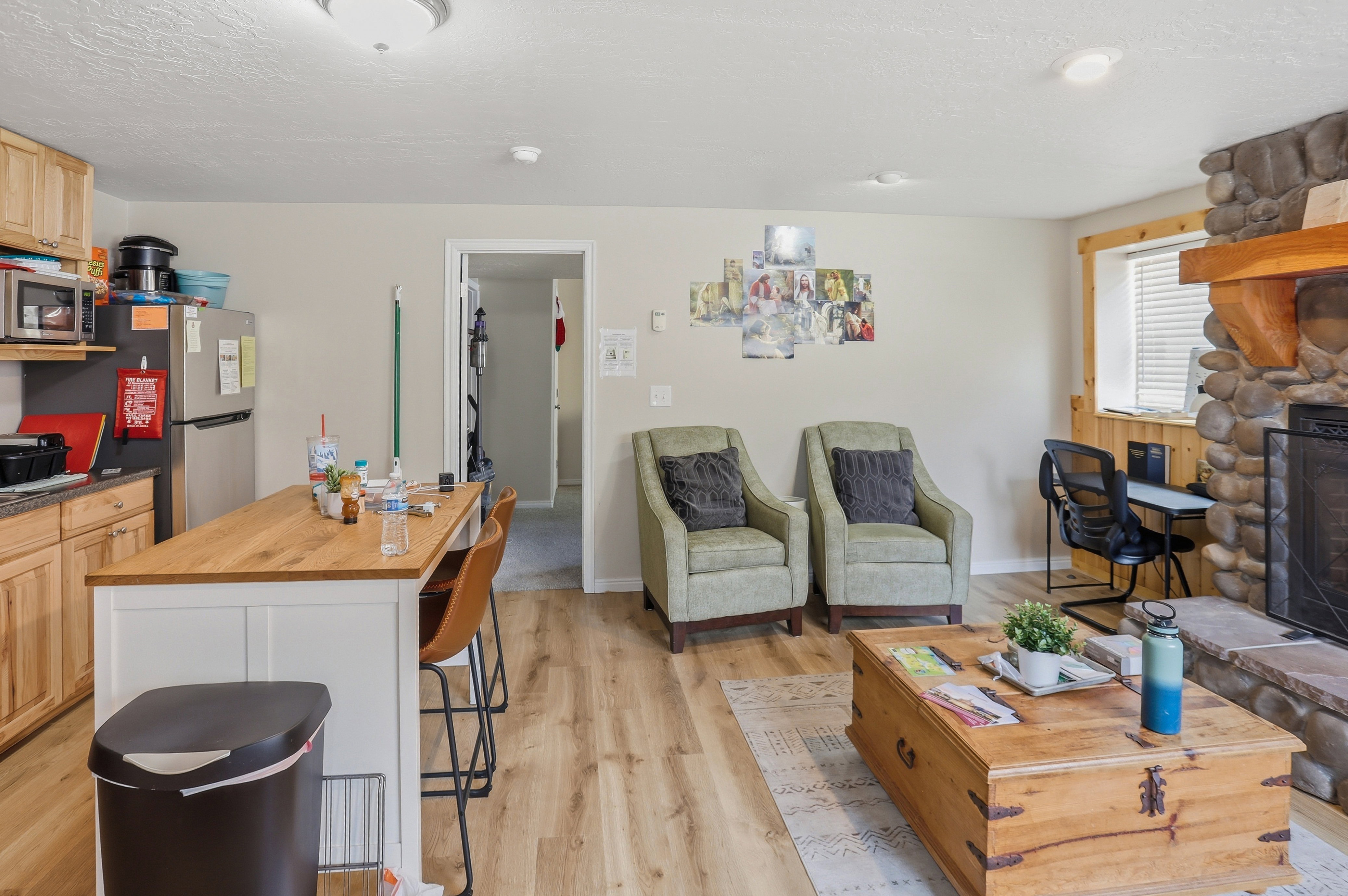 Open concept living space featuring wood-finish flooring, a stone-clad fireplace with a substantial wood mantel, and an integrated kitchen island with a wood countertop